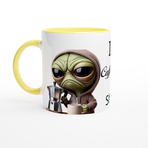 Puede incluir: Una taza de cerámica blanca con un borde amarillo presenta un extraterrestre de dibujos animados sosteniendo una cafetera y una taza de café. El texto en la taza dice "Me encanta la cafeína y tal vez 3 personas".