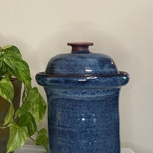 May include: A blue ceramic jar with a lid. The jar has a speckled texture and a dark brown rim and base. The lid has a small, rounded handle. The jar is approximately 10 inches tall.