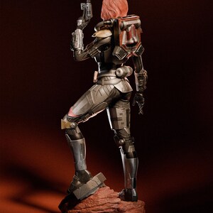May include: A detailed figurine of a female warrior in futuristic armor, holding a blaster pistol. The figure has red hair and a backpack with red accents. The armor is primarily gray and black, standing on a reddish-brown rock base.