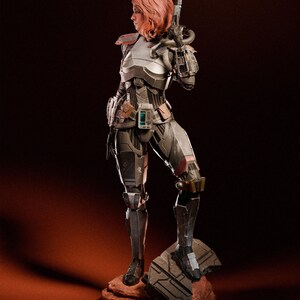 May include: A detailed statue of a female warrior in futuristic armor, holding a blaster rifle. The figure has short, reddish-pink hair and stands on a rocky base. The armor is primarily silver and gray with brown accents, and the overall design suggests a science fiction theme.