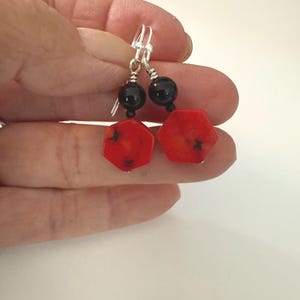 May include: A pair of dangle earrings featuring red, hexagonal beads with black accents, paired with black round beads. The earrings have silver-colored ear wires.