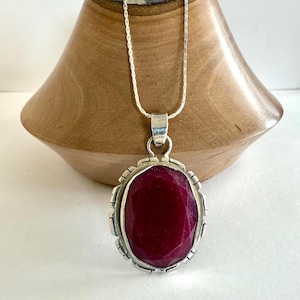 May include: A silver chain necklace with a pendant featuring a large, faceted, dark red gemstone set in a silver frame.