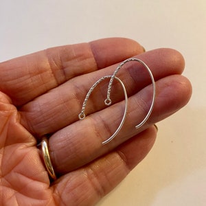 May include: Two silver earring hooks with a textured wire design. The hooks are curved and have a small loop at the top.