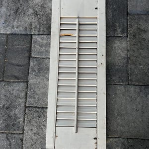 May include: White wooden shutters with a slatted design. The shutters are closed and have a rustic, weathered look.