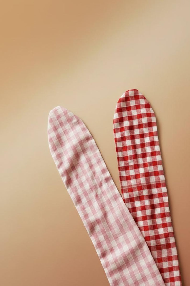 Puede incluir: Dos tiras de tela con estampado de cuadros vichy. Una tira es roja y blanca, la otra rosa y blanca. Las tiras est&aacute;n colocadas en diagonal sobre un fondo beige. La tela parece ser de algod&oacute;n o un material similar.
