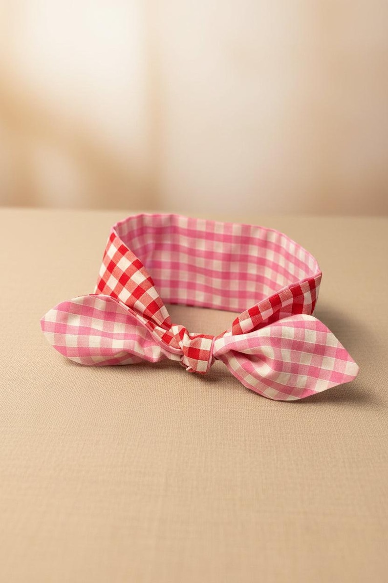 Puede incluir: Una diadema reversible con estampado de cuadros rosas y rojos. La diadema presenta un lazo anudado y un vichy rosa m&aacute;s claro en el reverso. La tela parece ser de algod&oacute;n.