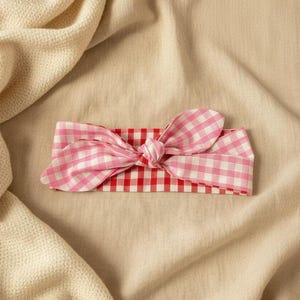 Puede incluir: Una diadema con estampado de cuadros rosas y blancos con un lazo anudado. La diadema se encuentra sobre un fondo beige neutro, creando una est&eacute;tica suave y femenina. Este accesorio es perfecto para a&ntilde;adir un toque de encanto a cualquier atuendo.