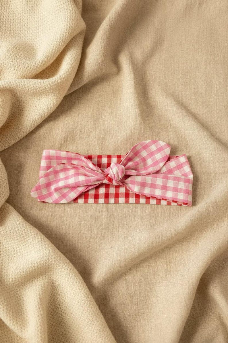 Puede incluir: Una diadema con estampado de cuadros rosas y blancos con un lazo anudado. La diadema se encuentra sobre un fondo beige neutro, creando una est&eacute;tica suave y femenina. Este accesorio es perfecto para a&ntilde;adir un toque de encanto a cualquier atuendo.