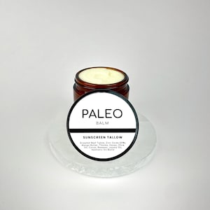 Puede incluir: Un tarro marrón con una etiqueta blanca que dice "PALEO BALM SUNSCREEN TALLOW" y enumera los ingredientes: Sebo de res alimentado con pasto, óxido de zinc (20%), manteca de mango, thonka, miel, aceite de oliva, cacao, cera de abejas, aceite de jojoba, mezcla de aceites estéticos.