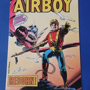 May include: A comic book cover featuring a superhero called Airboy, with the words "Airboy Reborn!" and "First Issue!" in red and yellow. The cover art shows Airboy in a red and blue costume, holding a machine gun, with a red and silver airplane in the background.