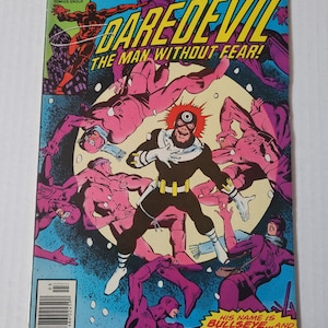 May include: A comic book cover featuring Daredevil, a superhero with red and black costume, fighting multiple enemies in a snowy landscape. The cover text reads "Daredevil The Man Without Fear!" and "His name is Bullseye...and he'll keep killing 'em till they're all dead!"
