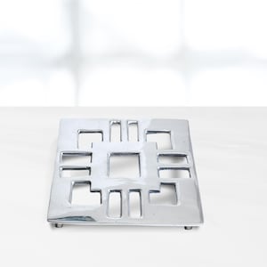 May include: A silver metal square hot pad with a geometric design of cut-out squares and rectangles.