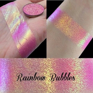 May include: A close-up of a pink iridescent eyeshadow with a rainbow sheen. The eyeshadow is labeled "Rainbow Bubbles".