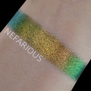 May include: A close-up of a green, gold, and blue eyeshadow swatch on skin. The text "NEFARIOUS" is visible in the image.