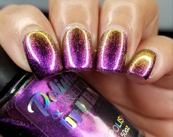 May include: A hand model wearing a purple and gold holographic nail polish. The nail polish bottle is labeled "Polish & Pretties by IMBA" and "Nail Polish 15ml / .50oz".