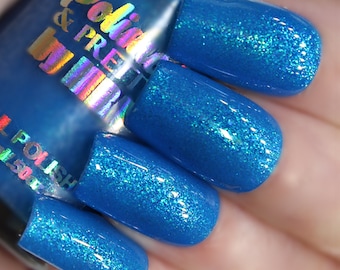 May include: Close-up of four fingernails painted with a bright blue nail polish with a fine iridescent glitter finish. The nail polish bottle is visible in the background with the brand name "Polish &  Pretties" printed on the label.