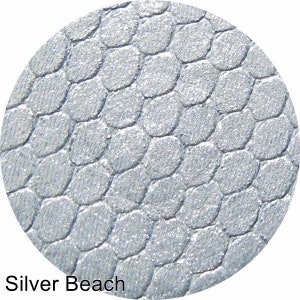 Puede incluir: Primer plano de una sombra de ojos plateada con un patrón texturizado similar a la piel de serpiente. La sombra de ojos está etiquetada como "Silver Beach".