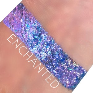 Puede incluir: Primer plano de una muestra de purpurina púrpura iridiscente con un brillo azul y plateado. La palabra "ENCHANTED" está escrita en blanco en la piel debajo de la purpurina.