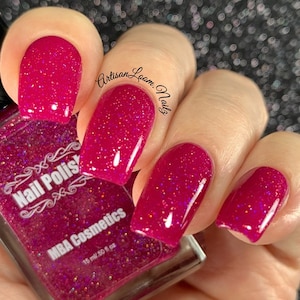 Può includere: Primo piano di una mano con smalto per unghie rosa con finitura glitterata. La bottiglia di smalto per unghie è etichettata "Nail Polish" e "MBA Cosmetics" con una dimensione di 15 ml / 0,50 fl oz.
