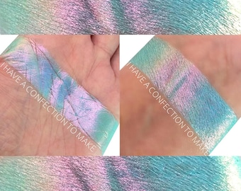 May include: A close-up of a light blue, green, and purple iridescent eyeshadow with a shimmery finish. The eyeshadow is swatched on a person's hand and the text "I HAVE A CONFECTION TO MAKE" is visible on the image.