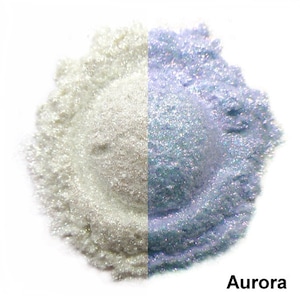 May include: A split image showcases two shimmering powders. One side is a bright, pearlescent white, while the other is a soft, iridescent blue-purple. The word "Aurora" is displayed in the bottom right corner. This product is likely used for crafts or cosmetics.