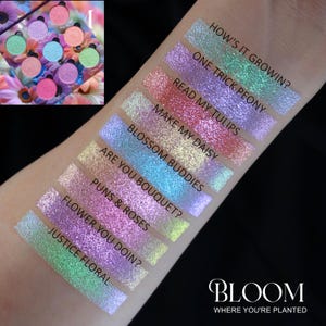 Könnte beinhalten: Nahaufnahme eines Arms mit neun schimmernden Lidschatten-Swatches mit Namen wie "Puns & Roses" und "Justice Floral". Eine kleine Lidschattenpalette befindet sich oben links. Der Markenname "BLOOM" befindet sich unten.