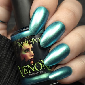 Può includere: Smalto per unghie metallizzato color teal e unghie dipinte. Il flacone di smalto è nero con le parole "NAIL POLISH" e "VENOM" stampate sopra, insieme al volto di una donna. Le unghie sono dipinte con uno smalto metallizzato teal.