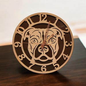 May include: A brown wooden clock with a white silhouette of a dog's face. The clock face has Roman numeral markings.