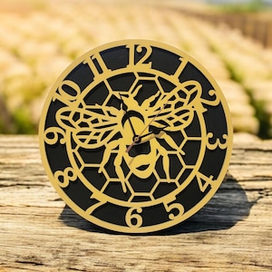 May include: A black and gold clock with a bee and honeycomb design. The clock face has Roman numerals and the bee is in the center of the honeycomb.