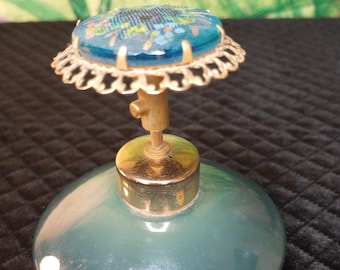 Könnte beinhalten: Eine vintage Parfümflasche aus blauem Glas mit goldenem Verschluss und einem floralen Design auf dem Stopfen.