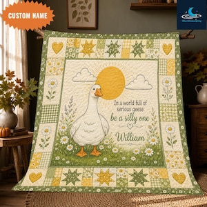 May include: A quilted blanket featuring a central illustration of a white goose standing in a field of daisies under a yellow sun. The text reads, In a world full of serious geese be a silly one William. The border has green and yellow patterns.