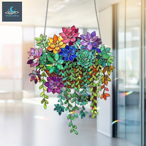 Puede incluir: Decoración colgante de planta suculenta colorida. La planta presenta una variedad de colores vibrantes, incluyendo rosa, morado, azul, verde y amarillo. Las hojas son detalladas y la planta está suspendida por una cadena. El diseño es llamativo y decorativo.