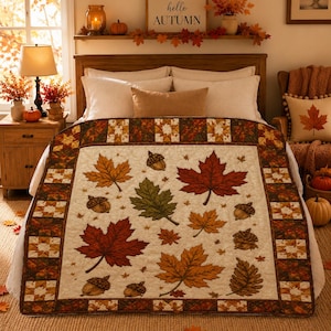 May include: A cream-colored quilt featuring a repeating pattern of autumn leaves in shades of red, orange, and green, interspersed with brown acorns. The quilt has a decorative border with a geometric patchwork design in warm fall colors.