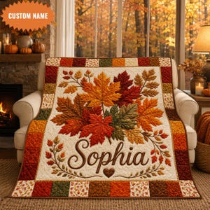 May include: A rectangular quilt featuring a central cream-colored panel with a vibrant arrangement of orange, red, and green autumn maple leaves. The name Sophia is printed in large brown script below the leaves, with a small heart icon.