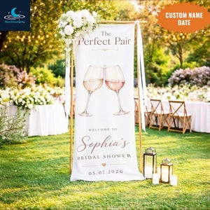 May include: A white banner with the text "The Perfect Pair" and two wine glasses, welcoming guests to Sophia's bridal shower on 05.07.2026. The banner is decorated with flowers and set up outdoors with lanterns and chairs.