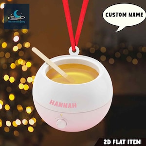 May include: A white and pink wax warmer with a red ribbon for hanging. The warmer contains a yellow liquid and a wooden applicator. The name "HANNAH" is printed on the front. A speech bubble reads "CUSTOM NAME".