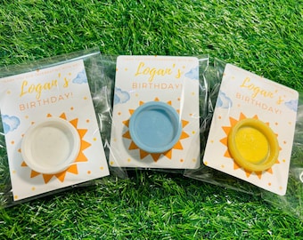 May include: Three party favor tags with the text "Logan's Birthday!" printed on them. Each tag has a different colored circle attached to it: white, blue, and yellow.