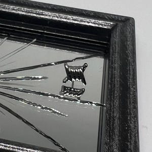 Puede incluir: Espejo cuadrado plateado con marco negro. El espejo presenta un diseño de rayos de sol con líneas radiales. Una pequeña pieza decorativa de metal, que se asemeja a alambre de púas, está adherida a la superficie del espejo.