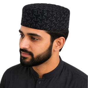 Op de afbeelding: Een donkerblauwe kufi-muts met een herhalend geometrisch patroon van in elkaar grijpende gebogen lijnen, gestikt met een lichtere draad. De cilindrische muts heeft een platte bovenkant en een gestructureerd ontwerp. De tekst Dark Blue is zichtbaar.