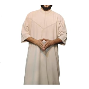 Può includere: Una camicia beige a maniche lunghe con colletto e scollo a V. La camicia ha un bordo decorativo lungo il collo e le maniche.