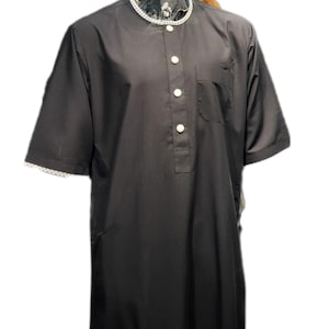 May include: A black short-sleeved tunic featuring a round neckline with a white and black checkered trim. The garment has a partial front button placket with four white buttons, a single chest pocket, and matching checkered trim on the sleeve cuffs.