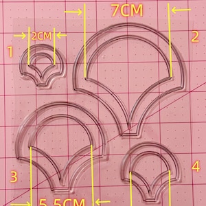 May include: Four clear plastic stencils with scalloped edges. The stencils are different sizes, with the largest measuring 7 inches by 5.5 inches and the smallest measuring 3.2 inches by 2 inches.