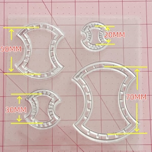 Peut inclure: Un ensemble de quatre moules en silicone transparent en forme de sablier avec des crêtes internes. Les moules sont étiquetés avec des dimensions de 20mm, 30mm, 50mm et 70mm, indiquant leurs tailles respectives. Chaque moule présente un bord cranté.