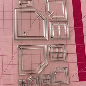 May include: A clear plastic sheet with nine different shapes and sizes of stencils. The stencils are labelled with letters A, B, C, D, and E. The stencils are designed for crafting and scrapbooking.