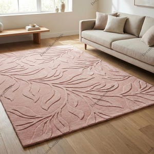 Könnte beinhalten: Ein großer, rechteckiger, rosafarbener Teppich mit einem erhabenen, blattartigen Muster. Der Teppich liegt auf einem Holzboden in einem Wohnzimmer, mit einem Sofa und einer Holzbank im Hintergrund.