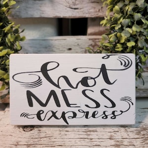 May include: White wooden sign with black calligraphy that reads "Hot Mess Express".
