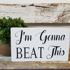 May include: White wooden sign with black text that reads "I'm Gonna BEAT This".
