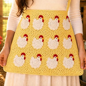 May include: A yellow crochet apron featuring a grid of twelve white chicken motifs. Each chicken has a red comb and wattle, and a yellow beak. The apron is constructed from square panels, with each panel containing one crocheted chicken figure.
