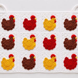May include: A white crocheted potholder featuring a grid pattern with twelve individual squares. Each square contains a crocheted chicken in brown, red, or yellow with a red comb. The potholder has two white loop handles.
