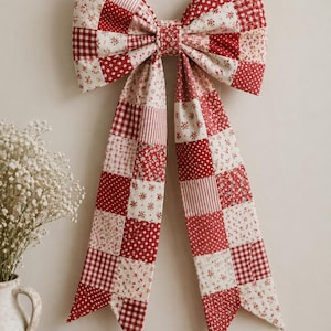 May include: A large, decorative bow made of patchwork fabric, featuring red and white patterns including polka dots, floral prints, and gingham. The bow is mounted on a neutral wall, with long, flowing tails.